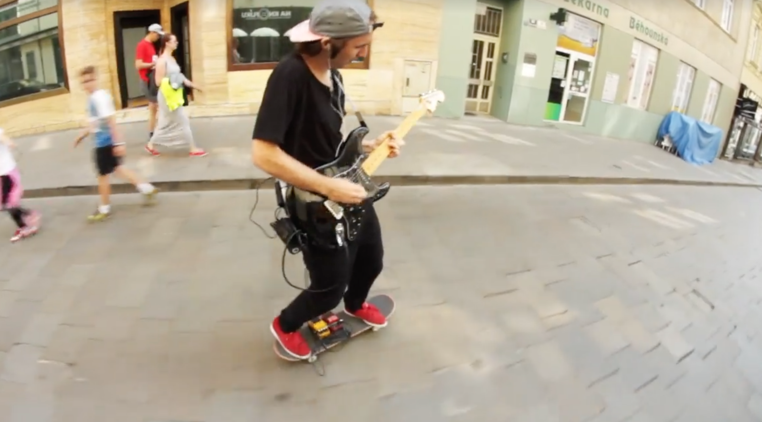 Il joue de la guitare en faisant du skateboard
